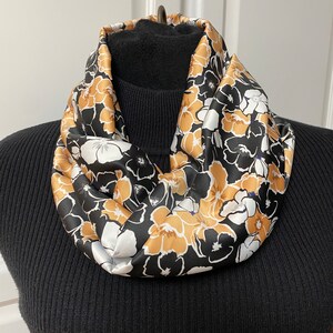 May include: A black, white, and gold floral print infinity scarf. The scarf is made of a silky material and is a great accessory for any outfit.