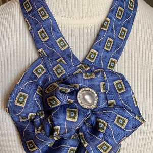 May include: A blue and gold patterned necktie with a pearl and rhinestone brooch, tied into a bow.
