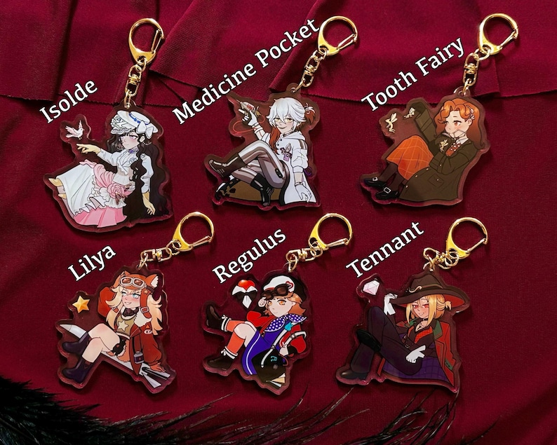 Peut inclure: Six porte-cl&eacute;s en acrylique repr&eacute;sentant des personnages de style anime avec des anneaux dor&eacute;s. Les personnages incluent Isolda, Medicine Pocket, Tooth Fairy, Lilya, Regulus et Tennant. Chaque personnage est repr&eacute;sent&eacute; dans une pose et une tenue uniques, avec des couleurs vives et des motifs d&eacute;taill&eacute;s.