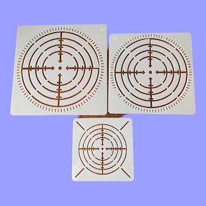 May include: Three white plastic stencils featuring a target design. The stencils are of varying sizes and have concentric circles with a crosshair in the centre.