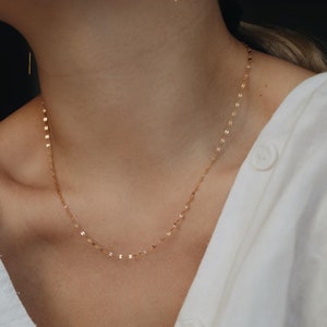 Könnte beinhalten: Eine zarte goldene Kettenkette mit einem schlichten, minimalistischen Design. Die Kette besteht aus kleinen, miteinander verbundenen ovalen Formen.