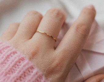 Puede incluir: Una mano con un suéter de punto rosa sostiene una pequeña caja de regalo rosa. Se lleva un fino anillo de oro en el dedo índice.