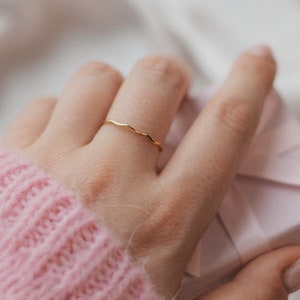 Peut inclure: Une main portant un pull en tricot rose tient une petite boîte cadeau rose. Une fine bague en or est portée à l'index.