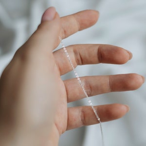 May include: A silver chain necklace, held in a hand, against a white background.