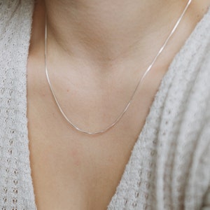 May include: A silver chain necklace on a person wearing a white sweater.