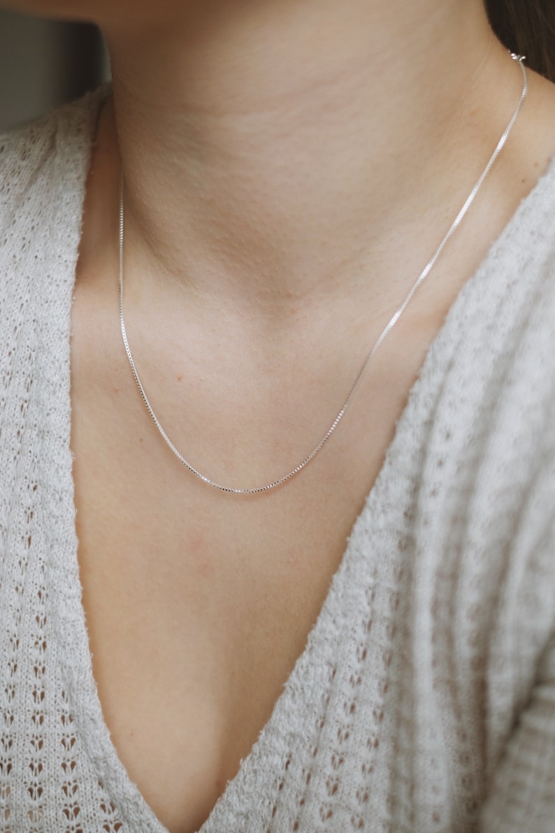 May include: A silver chain necklace on a person wearing a white sweater.