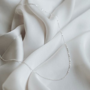 May include: A delicate silver chain necklace on a white fabric background.
