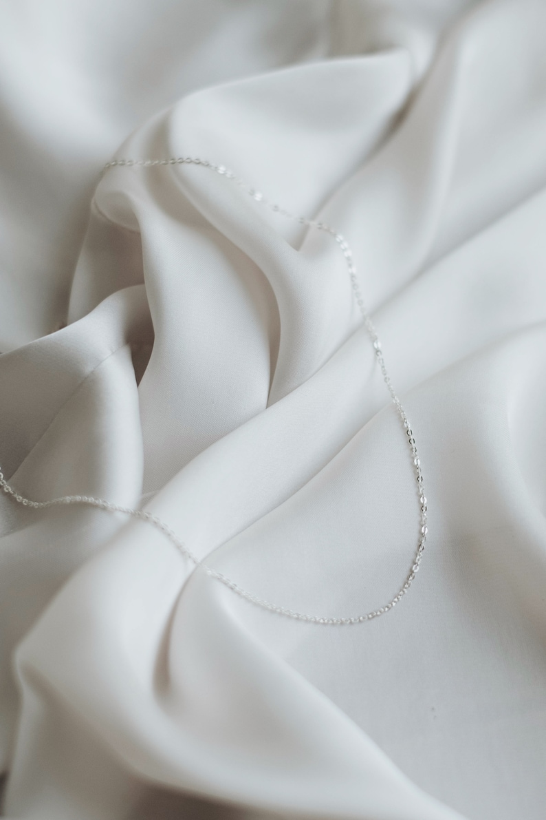 May include: A delicate silver chain necklace on a white fabric background.