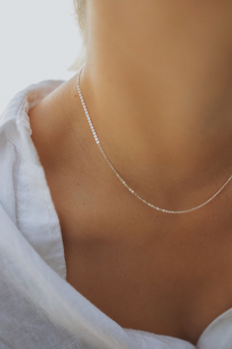 May include: A delicate silver chain necklace on a person's neck. The chain is thin and has a simple design.
