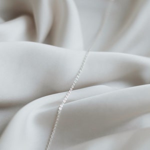 May include: A silver chain necklace on a white fabric background.