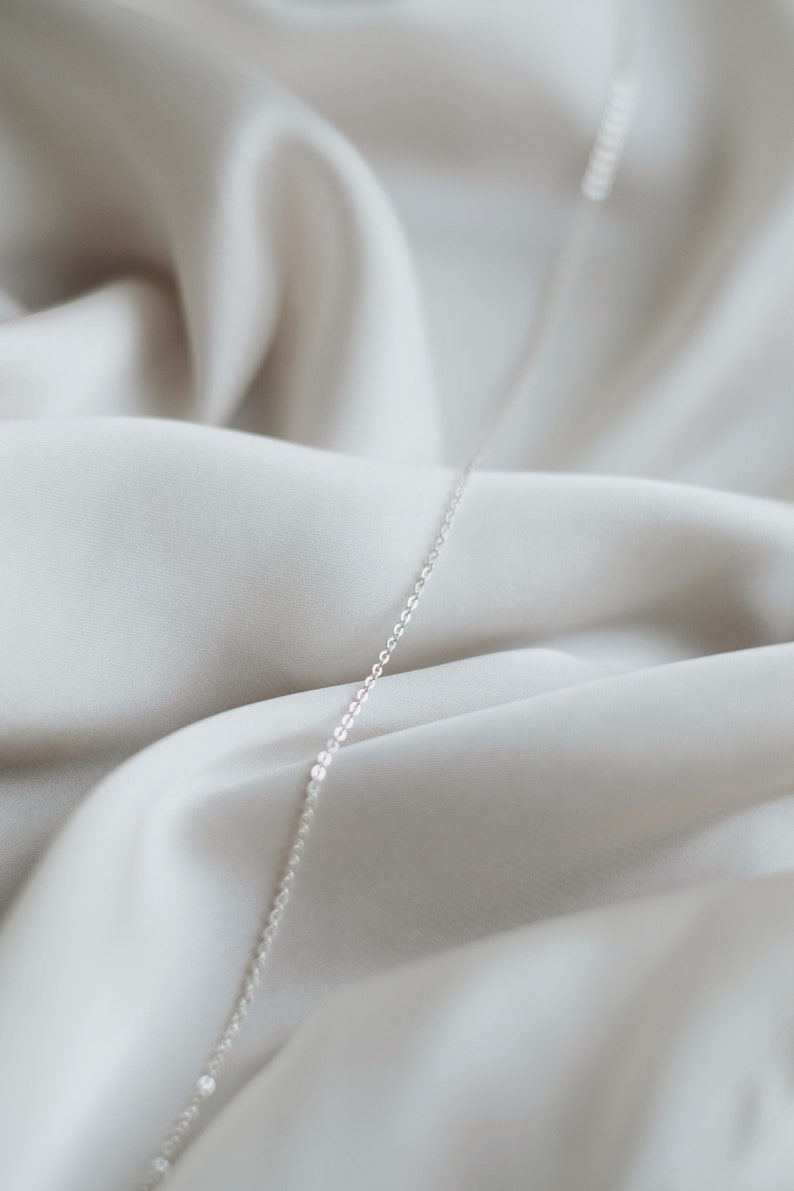 May include: A silver chain necklace on a white fabric background.