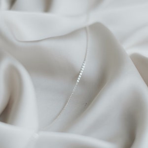 May include: A delicate silver chain necklace on a white fabric background.