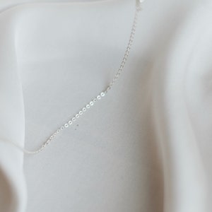 May include: A silver chain necklace on a white fabric background.