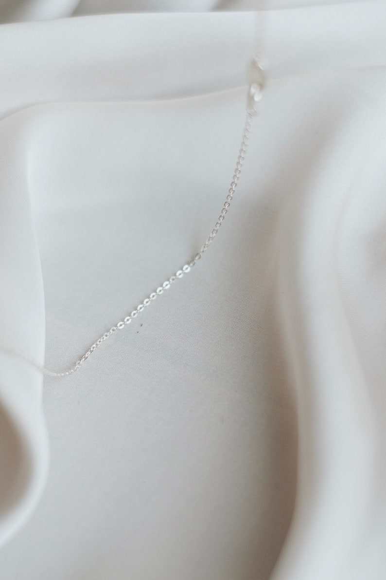 May include: A silver chain necklace on a white fabric background.