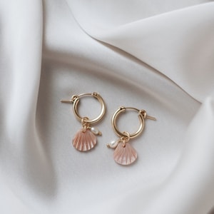 Op de afbeelding: Gouden creolen met een roze schelpbedel en een witte parel accent.