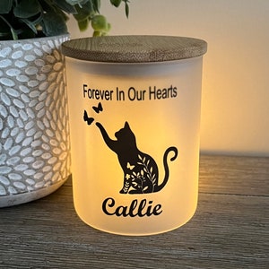 May include: White ceramic candle jar with a bamboo lid. The jar has a black silhouette of a cat with butterflies and the text "Forever In Our Hearts" and "Callie".