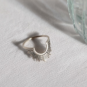 May include: A silver ring with a sunburst design. The ring is open in the back and has a delicate, intricate design.