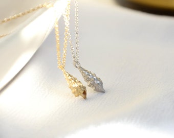May include: Two delicate necklaces with a leaf-shaped pendant. One necklace is gold and the other is silver. The necklaces are hanging from a white surface.