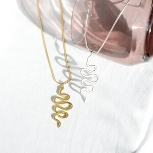 Peut inclure: Deux colliers de serpent en or et en argent avec un pendentif en forme de serpent enroulé. Les colliers sont présentés sur un fond en tissu blanc.