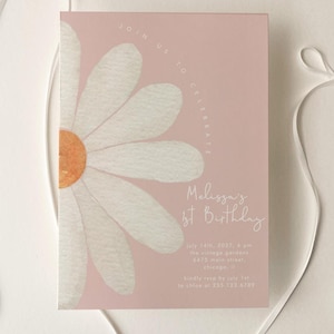 May include: A rectangular invitation card with a dusty pink background featuring a large white daisy illustration with an orange center. The text reads Melissa's 1st Birthday, along with date and location details. Two white satin ribbons frame the card.