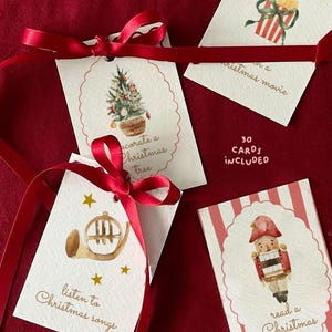 May include: A set of white rectangular cards with red satin ribbons, featuring watercolour illustrations of a gingerbread house, popcorn, a Christmas tree, a French horn, and a nutcracker, with text including 30 CARDS INCLUDED.