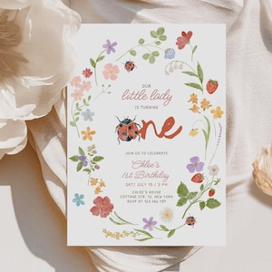 May include: A rectangular birthday invitation card featuring a watercolour floral wreath with ladybugs and strawberries. The text reads: Our little lady is turning one, join us to celebrate Chloe's 1st Birthday, Sat July 15, 3 PM, Chloe's House.