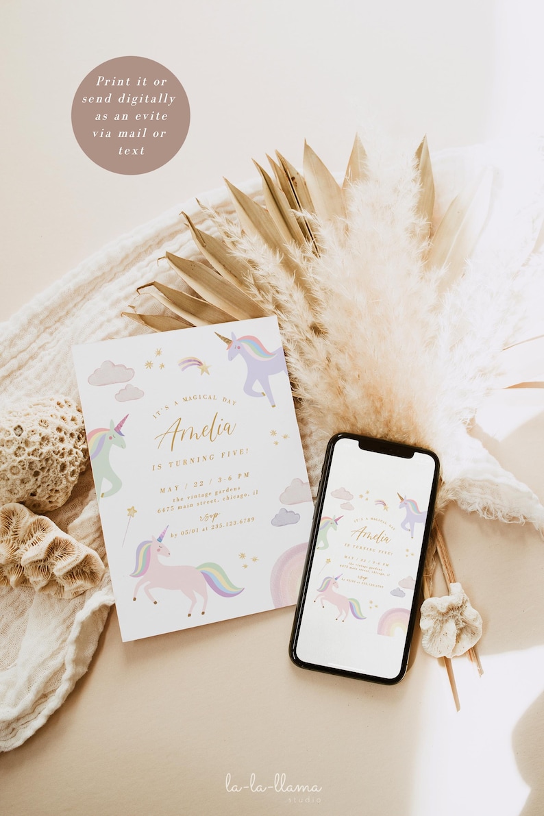 May include: A white invitation card with a unicorn theme. The card features a pink unicorn with a rainbow mane and tail, surrounded by clouds and stars. The text on the card reads "It's a magical day Amelia is turning five!" with the date and time of the event. The card is displayed on a white surface with a bouquet of dried pampas grass.