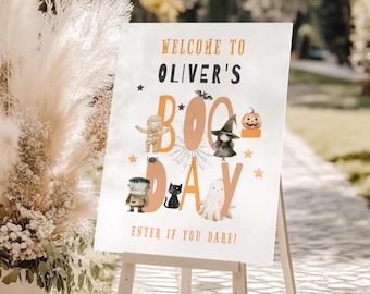 Puede incluir: Un letrero blanco sobre un caballete de madera con las palabras "Welcome to Oliver's Boo Day" en naranja y negro. El letrero presenta ilustraciones de personajes de Halloween. El texto "Enter if you dare!" está en la parte inferior.