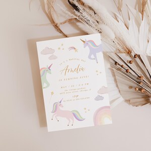 May include: A white invitation card with a rainbow and unicorn theme. The text on the card reads "It's a magical day Amelia is turning one. May 22, 2:00 PM. The unicorn garden 123 Main Street, Chicago, IL 60601. RSVP to 123-456-7890."
