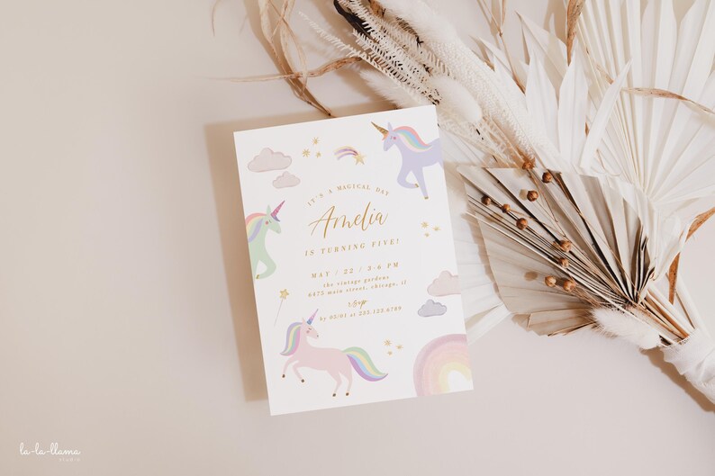 May include: A white invitation card with a rainbow and unicorn theme. The text on the card reads "It's a magical day Amelia is turning one. May 22, 2:00 PM. The unicorn garden 123 Main Street, Chicago, IL 60601. RSVP to 123-456-7890."