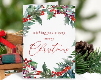 May include: A white Christmas card featuring a watercolour illustration of a holly wreath with red berries. The text "Wishing you a very merry Christmas" is written in red cursive.