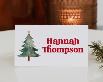 May include: A white place card with a green watercolor Christmas tree and the name "Hannah Thompson" in red text.