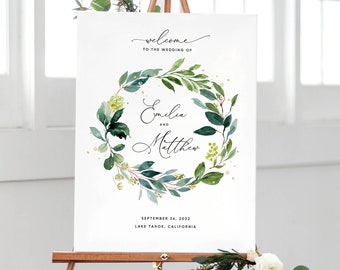 May include: A white wedding welcome sign with a green and gold wreath featuring the names "Emilia and Matthew" and the date "September 26, 2022" and location "Lake Tahoe, California".