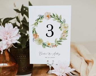 Pode incluir: Um cartão branco com um design de coroa de flores e o número 3 no centro. O cartão também inclui o texto "Caroline & Anthony" e a data "09.21.202X". O cartão é exibido em um suporte de madeira.