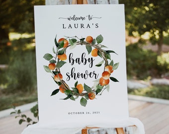 May include: Welcome to Laura's baby shower sign with a wreath of orange blossoms and leaves. The sign says "Welcome to Laura's Baby Shower" and "October 26, 2021".