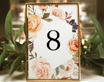 May include: A gold-framed table number card with a floral design featuring peach, white, and purple flowers. The number 8 is displayed in a black hexagon in the center of the card.