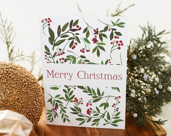 May include: A white Christmas card with a red "Merry Christmas" greeting and a pattern of green leaves and red berries.