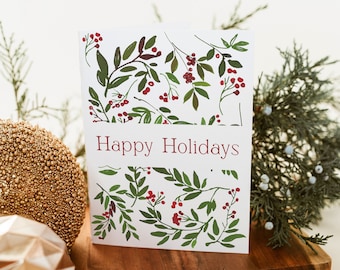 May include: A white card with a green and red floral pattern and the text "Happy Holidays". The card is sitting on a wooden surface.