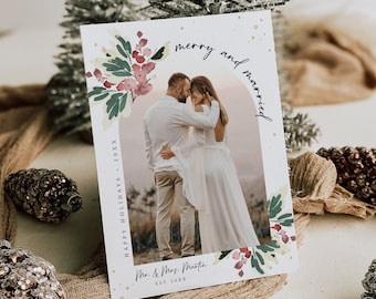 May include: A Christmas card with a watercolor floral design and a photo of a couple. The card says "Merry and Married" and "Mr. & Mrs. Martin Est. 20XX" with a gold glitter background.