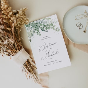 May include: Wedding invitation with a watercolor design of green eucalyptus leaves and white dots. The text reads "Welcome to the wedding of Stephanie and Michael, September 21, 2019, Wine & Roses | Lodi, California".