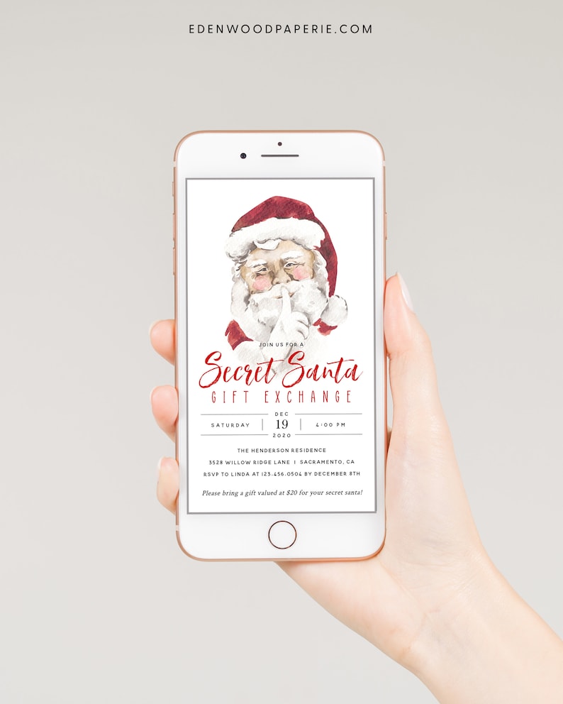 以下が含まれることがあります： スマートフォンには、Secret Santaのギフト交換の招待状が表示されています。招待状には、唇に指を当てたサンタクロースの水彩イラストが描かれています。テキストにはイベントの詳細が含まれています。