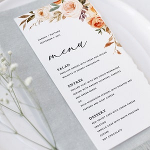 May include: A wedding menu card with a floral design featuring peach, orange, and white flowers. The menu includes salad, entree, and dessert options. The text on the card reads "Hannah + Matthew, September 7, 2021".