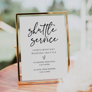 May include: A gold-framed sign with white paper and black text that reads "Shuttle Service" with a heart symbol and the text "Complimentary Wedding Shuttle" with the times "To Wedding from Hotel 3:30-4:00PM" and "To Hotel from Wedding 9:00-9:30PM".