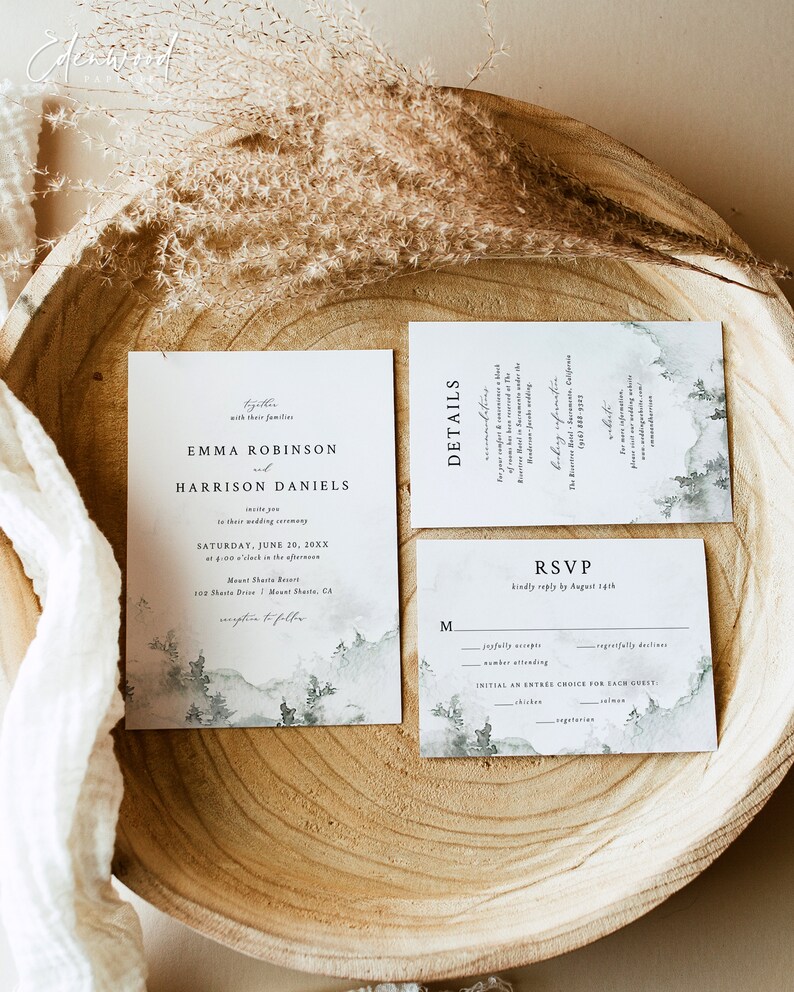May include: Wedding invitation suite with a watercolor background featuring a mountain range and trees. The invitation card is white with black text and reads "Emma Robinson and Harrison Daniels" with the wedding date and location. The RSVP card is white with black text and includes a section for guests to indicate their attendance and meal choice.