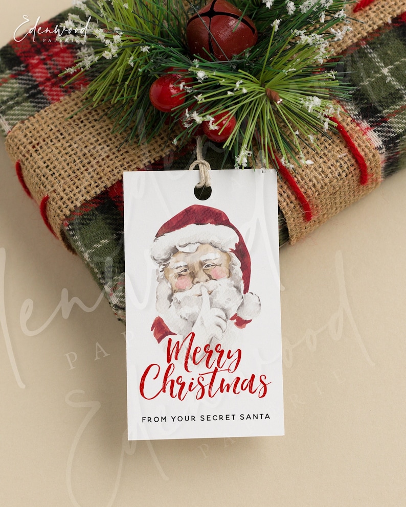 May include: White gift tag with a watercolor illustration of Santa Claus with his finger to his lips. The text reads "Merry Christmas" in red lettering and "From your Secret Santa" in black lettering.