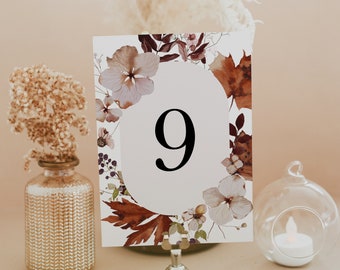 May include: A white card with a floral design and the number 9 printed in black. The card is on a gold metal stand and is surrounded by decorative elements.