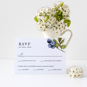 May include: A white RSVP card with black text and a watercolor illustration of blueberries. The text reads "RSVP by April 28th". The card has a line for the guest to initial their choice of entree: chicken, salmon, or vegetarian.