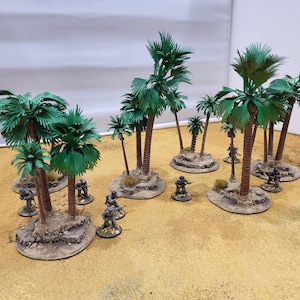 Puede incluir: Palmeras en miniatura con hojas verdes y troncos marrones sobre pequeñas bases texturizadas. Varios soldados en miniatura están colocados alrededor de los árboles sobre una superficie beige.