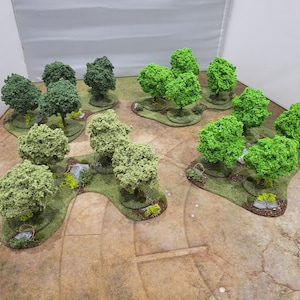 Puede incluir: Piezas de terreno en miniatura con grupos de árboles verdes sobre bases cubiertas de hierba. Los árboles tienen copas texturizadas y redondeadas. Algunas bases incluyen pequeñas rocas y arbustos. Ideal para juegos de mesa o exhibiciones de modelos.
