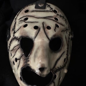 May include: A white hockey mask with black stitching and holes. The mask has a distressed look and is painted to look like a face. The mask is a popular Halloween costume accessory.